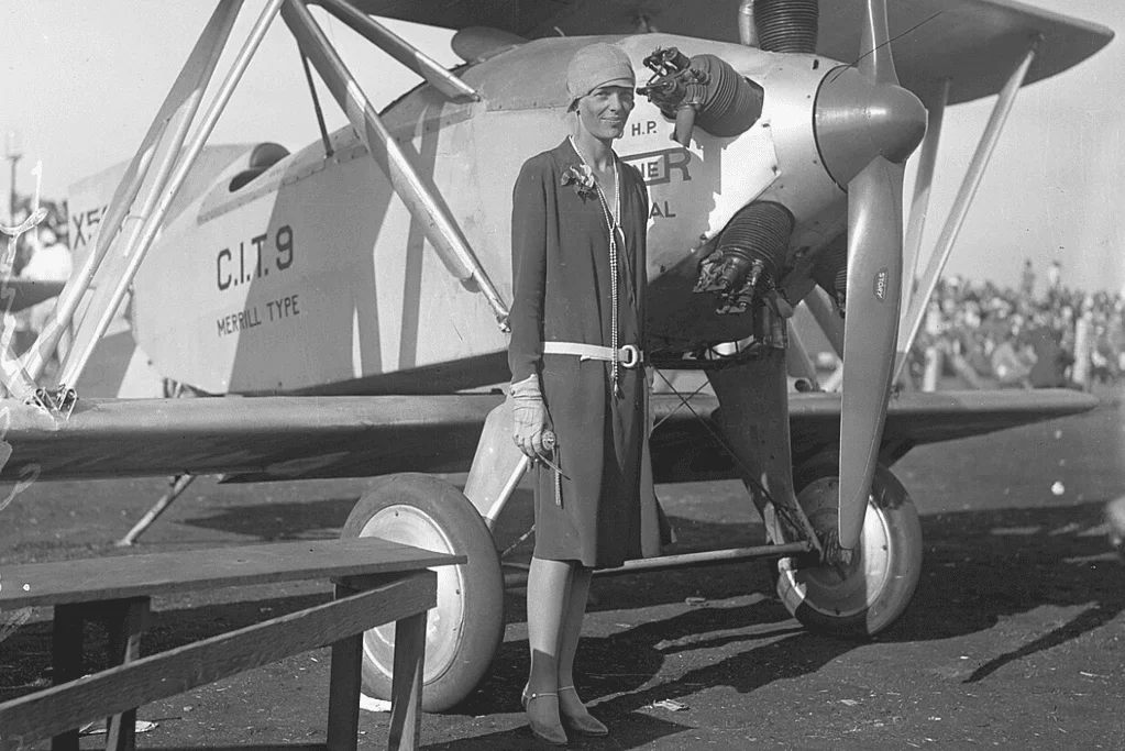 Image of Amelia Earhart posing in front of a biplane for a blog post about early pioneers of aviation.